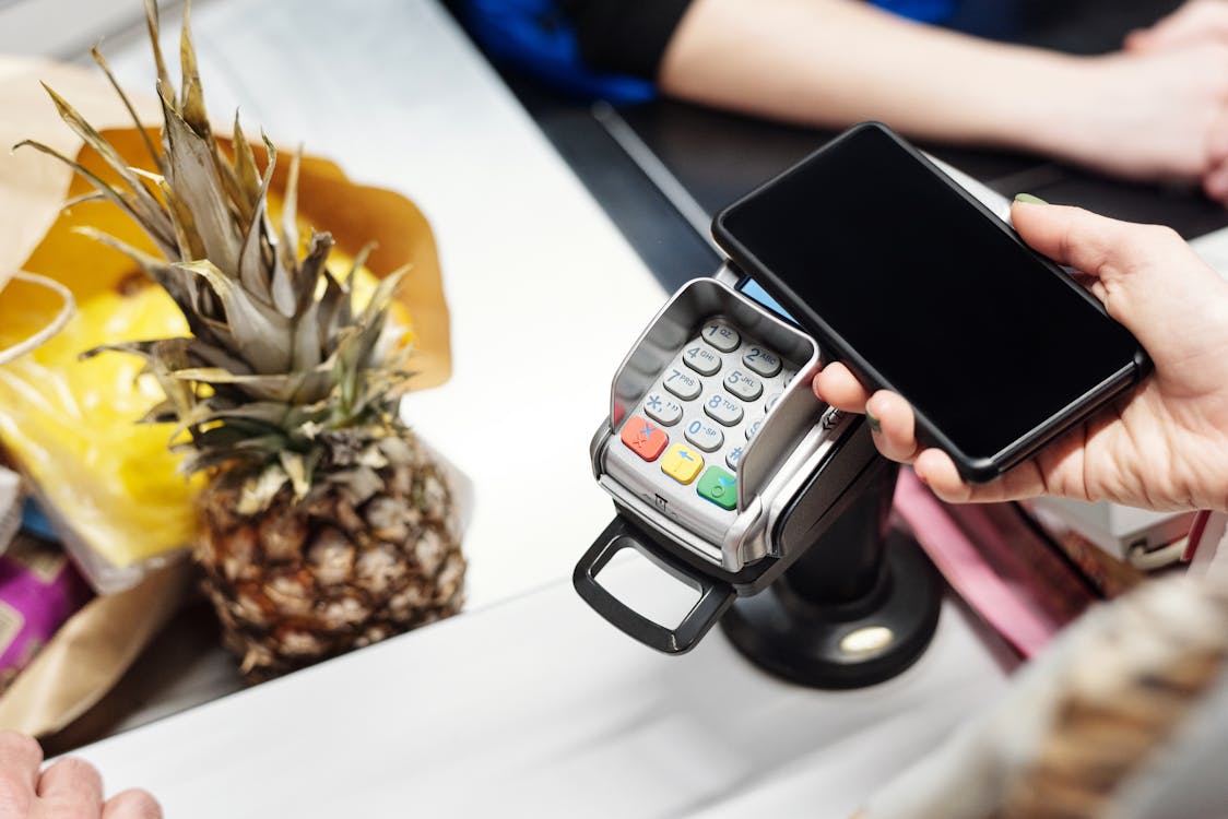 A person tapping a smartphone on a contactless payment terminal at a retail counter to complete a mobile wallet transaction.