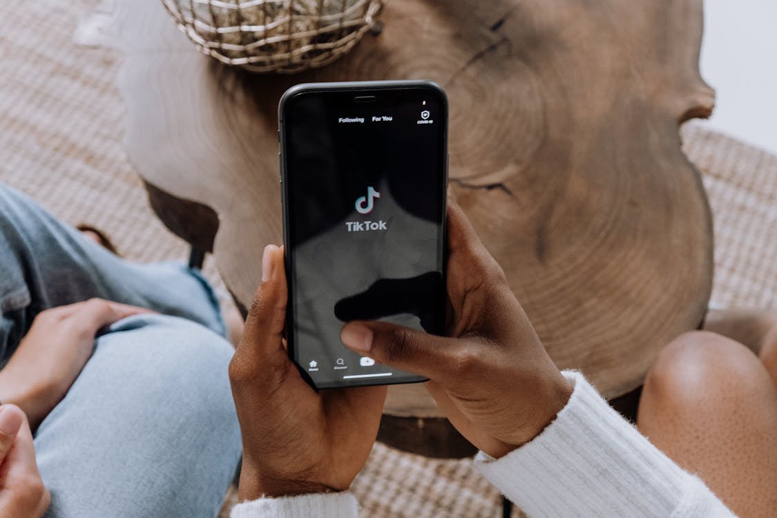 A person holding a black Android smartphone showing a mobile app interface on a wooden surface.