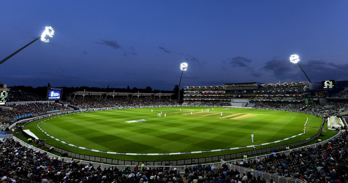 A floodlit cricket stadium packed with spectators watching a T20 match at dusk on a bright green pitch.